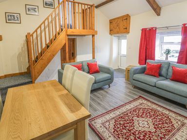 A living room with two gray sofas with red cushions and a wooden table near stairs at Crud yr Awel in Braichmelyn near Bethesda