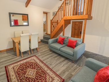 A living room with blue sofas red cushions wooden staircase dining table with cream chairs and a decorative rug at Crud yr Awel in Braichmelyn near Bethesda