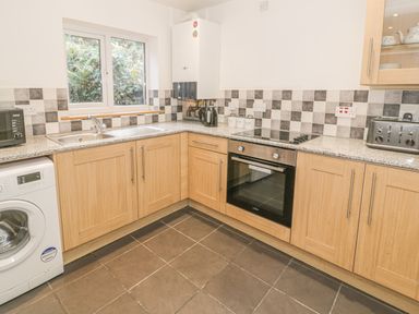 A kitchen with wooden cabinets a washing machine a microwave a toaster a kettle and a window at Crud yr Awel in Braichmelyn near Bethesda