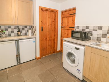 A kitchen with wooden cabinets washing machine microwave two fridges and two wooden doors at Crud yr Awel in Braichmelyn near Bethesda