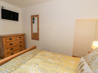 A bedroom with a wooden bed, floral bedding, wooden dresser, wall mirror, and wall-mounted TV at Crud yr Awel in Braichmelyn near Bethesda