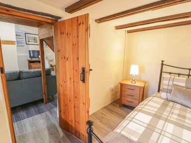 A bedroom with a bed a bedside table with a lamp and an open wooden door showing a living room with a sofa and a television at Crud yr Awel in Braichmelyn near Bethesda