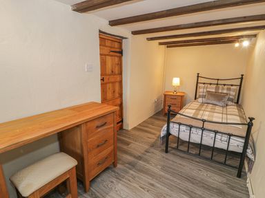 A bedroom with a single bed a wooden desk with drawers and a stool a wooden door and exposed ceiling beams at Crud yr Awel in Braichmelyn near Bethesda