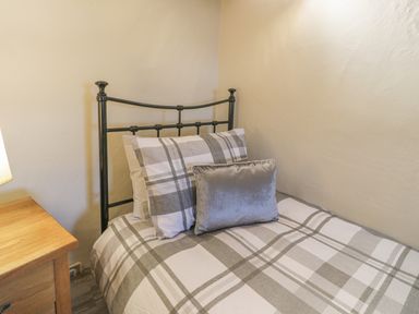 A bedroom with a metal framed single bed with plaid bedding and pillows next to a wooden nightstand with a lamp at Crud yr Awel in Braichmelyn near Bethesda