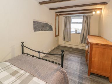 A bedroom with a metal bed frame wooden dresser window with curtains and wooden beams on the ceiling at Crud yr Awel in Braichmelyn near Bethesda