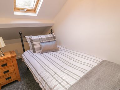 A single bed with striped bedding next to a wooden nightstand with a lamp under a skylight window at Crud yr Awel in Braichmelyn near Bethesda