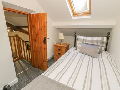 A bedroom with a single bed a bedside table with a lamp a wooden door and a skylight window at Crud yr Awel in Braichmelyn near Bethesda