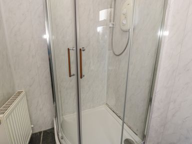 A shower enclosure with glass doors a shower unit and a radiator on a wall at Crud yr Awel in Braichmelyn near Bethesda