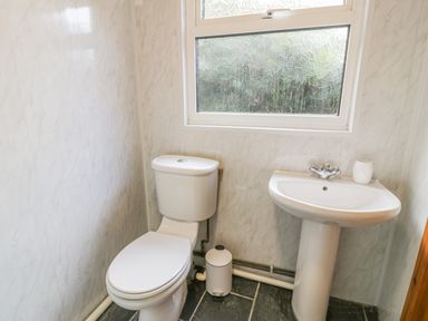 A bathroom with a toilet a pedestal sink a small trash can and a frosted window at Crud yr Awel in Braichmelyn near Bethesda