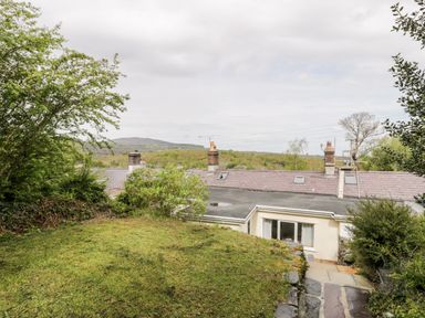 A backyard with grass and bushes overlooking rooftops and trees at Crud yr Awel in Braichmelyn near Bethesda