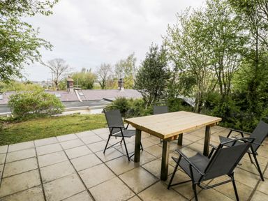 An outdoor patio with a wooden table and four black chairs surrounded by trees at Crud yr Awel in Braichmelyn near Bethesda