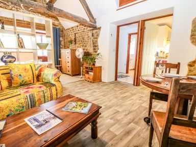A living room with a wooden coffee table and a colorful sofa with a bookshelf behind at The Forge at Smithy Cottage in Bloxham