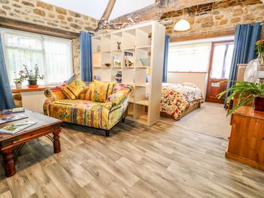 A studio room with a colorful sofa a wooden coffee table a bed separated by a cubed bookshelf and stone walls at The Forge at Smithy Cottage in Bloxham