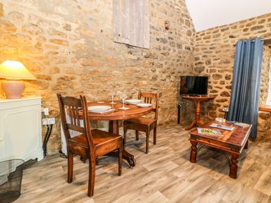 A small dining area with a wooden table set for two and a sitting area with a coffee table and television in a room with stone walls