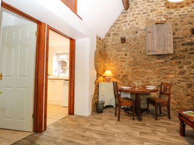 A dining area with a round wooden table set with plates and glasses two wooden chairs a lamp on a white cabinet and a stone wall at The Forge at Smithy Cottage in Bloxham