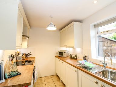 A kitchen with wooden countertops white cabinets tile floor and a window at The Forge at Smithy Cottage in Bloxham