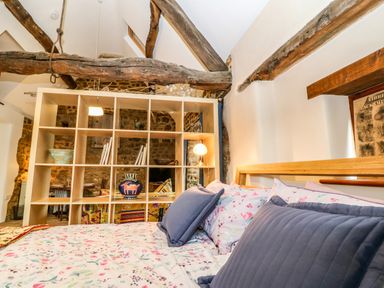 A bedroom with floral bedding and blue pillows next to a wooden shelf and stone walls at The Forge at Smithy Cottage in Bloxham