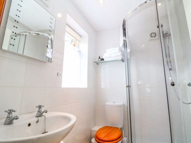 A bathroom with a sink mirror toilet with wooden lid glass shower and towels on a shelf at The Forge at Smithy Cottage in Bloxham