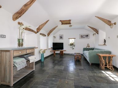 A living room with a green sofa a wooden side table a TV on a wooden stand and wooden ceiling beams at Harbour Cottage in Boscastle