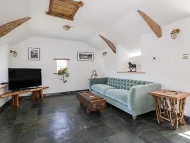 A living room with a green sofa wooden coffee table wooden side table and television on a wooden stand at Harbour Cottage in Boscastle