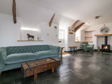 A living room with green sofa and armchair wooden chest coffee table wood burning stove and wooden beams at Harbour Cottage in Boscastle