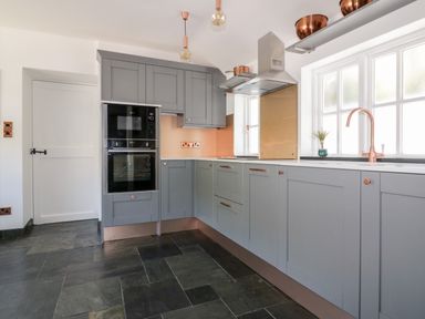 A kitchen with grey cabinets black double oven copper fixtures and dark tile floor at Harbour Cottage in Boscastle