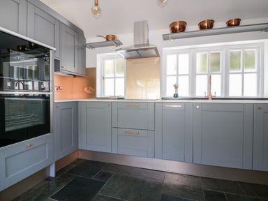 A kitchen with grey cabinets copper handles copper pots and utensils on shelves and slate flooring at Harbour Cottage in Boscastle