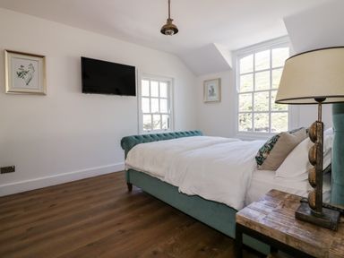A bedroom with a teal upholstered bed white bedding wooden floor TV on the wall and a bedside table with a lamp at Harbour Cottage in Boscastle