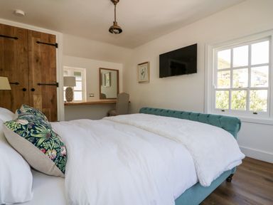 A bedroom with a bed a window a wall mounted television a wooden wardrobe and a desk with a chair at Harbour Cottage in Boscastle