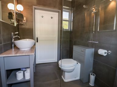 A bathroom with a sink on a wooden counter a toilet a toilet paper holder and a window at Harbour Cottage in Boscastle