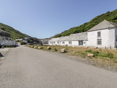 A paved road with white buildings on one side and green hills in the background at Harbour Cottage in Boscastle