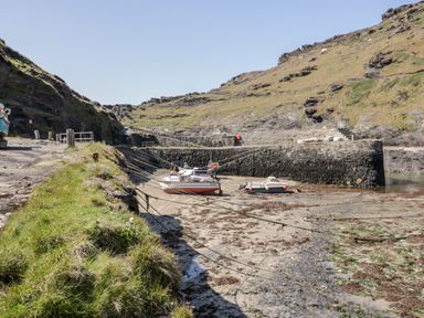 A small harbor with boats on the sand surrounded by rocky hills and a stone wall at Harbour Cottage in Boscastle