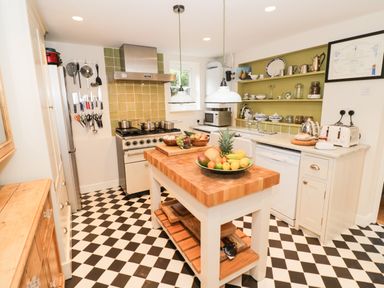 A kitchen with a wooden island table and fruit bowls and pots on gas stove at Prospect Cottage in Malvern Wells near Great Malvern