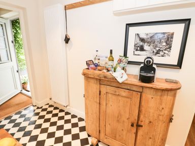 A wooden cabinet with snacks and a coffee machine on top in a room with checkered floor tiles and an open door