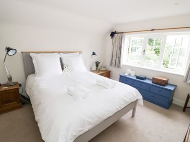 A bedroom with a bed made with white linens a small teddy bear on the bed bedside tables with lamps a blue dresser under a window at Prospect Cottage in Malvern Wells near Great Malvern