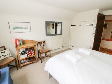 A bedroom with a white bed, wooden chairs, a small wooden table with books and a box with a union jack design at Prospect Cottage in Malvern Wells near Great Malvern