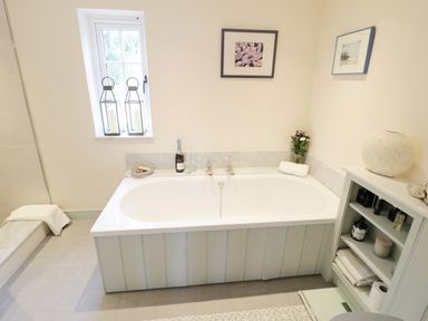A bathroom with a bathtub a window with candles a cabinet with towels and toiletries at Prospect Cottage Malvern Wells near Great Malvern