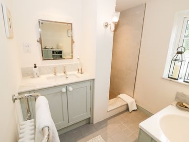 A bathroom with a sink cabinet mirror towel rack shower window and lantern candles at Prospect Cottage Malvern Wells near Great Malvern