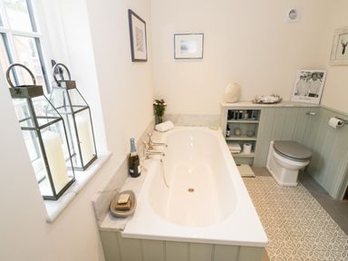 A bathroom with a bathtub, toilet, candles in lanterns, and shelves with toiletries at Prospect Cottage Malvern Wells near Great Malvern