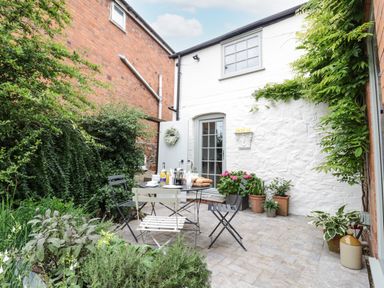 An outdoor patio with a table and chairs surrounded by plants and flowers at Prospect Cottage in Malvern Wells near Great Malvern