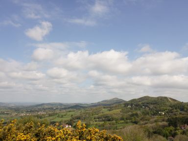 A landscape with hills trees and yellow flowers under a partly cloudy sky at Prospect Cottage in Malvern Wells near Great Malvern