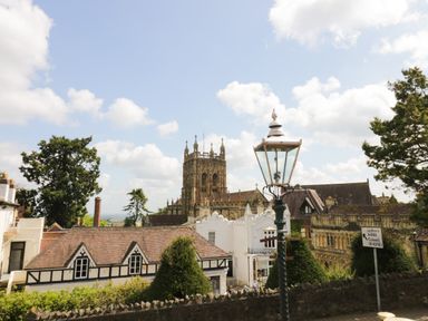 A street view of buildings with a church tower and a lamp post near a road sign at Prospect Cottage in Malvern Wells near Great Malvern