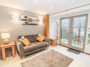 A living room with a sofa cushions table lamp and glass doors opening to a balcony at Lowe-McConnell in Far Sawrey