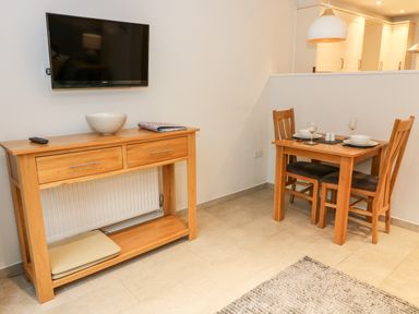 A dining area with a small wooden table set for two and a wooden console table with a wall-mounted television above at Lowe-McConnell in Far Sawrey