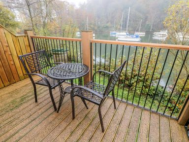 A balcony with two metal chairs and a metal table overlooking a river with boats and trees at Lowe-McConnell in Far Sawrey