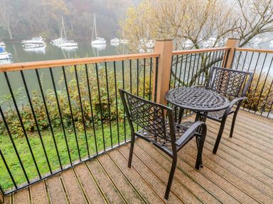 A balcony with two metal chairs and a round metal table overlooking a body of water with boats at Lowe McConnell in Far Sawrey