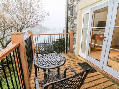 A small balcony with metal table and chairs overlooking a foggy lake with boats at Lowe McConnell in Far Sawrey
