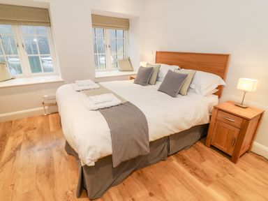 A bedroom with a double bed pillows folded towels bedside table with lamp and two windows at Lowe-McConnell in Far Sawrey