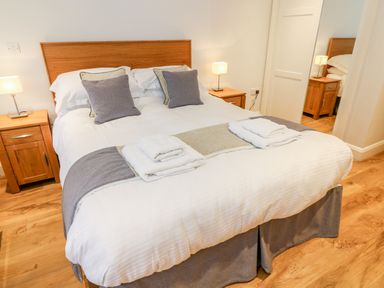 A bedroom with a double bed with pillows and towels bedside tables with lamps and wooden flooring at Lowe-McConnell in Far Sawrey