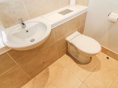 A bathroom with a white sink and a toilet with beige tiled walls and floor at Lowe-McConnell in Far Sawrey